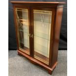 A mahogany two door display cabinet, slightly bowed oversailing top, brass tubular lined doors,