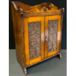 An early 20th century oak smoker's cabinet, shaped cresting, pair of carved panel doors enclosing