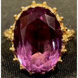 A 9ct gold dress ring, set with a large faceted oval amethyst stone, pierced openwork bezel, scrolls