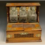 An Edwardian oak three bottle tantalus, silver plated oak case, three cut glass decanters, lidded