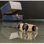 A sapphire and diamond ring, set with three deep blue oval sapphires each divided by a pair og old