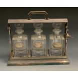 An early 20th century plated three bottle tantalus, clear glass decanters, decanter labels,