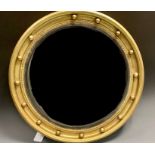 A Regency design giltwood and gesso circular convex looking glass, reeded ebonised bezel, surmounted