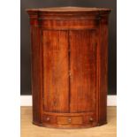 A George III mahogany crossbanded oak bowfront corner cupboard, moulded cornice above a pair of