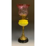 A Victorian brass and yellow milk glass oil lamp, cranberry glass shade above relief decorated