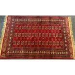 A Bohkara type rug, central three rows of geometric medallions, within multi band border, deep red