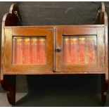 An early 20th century oak wall hanging glazed bookcase, complete with twelve volumes of
