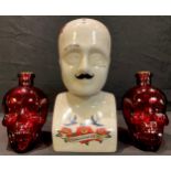A pair of red glass bottles each in the form of a human skull, 17cm high; a novelty phrenology bust,