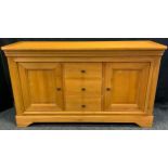 A golden tone light oak sideboard, oversailing top above three central drawers and two cupboard