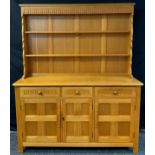An Ercol style light oak dresser, the top with two teirs of shelving, above a base with three