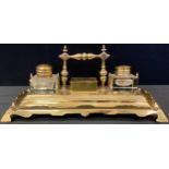 An early 20th century brass standish, central stamp box, flanked by two clear glass wells, the