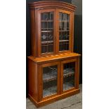 An Arts & Crafts walnut display cabinet, arched pediment above two leaded stained and clear glass