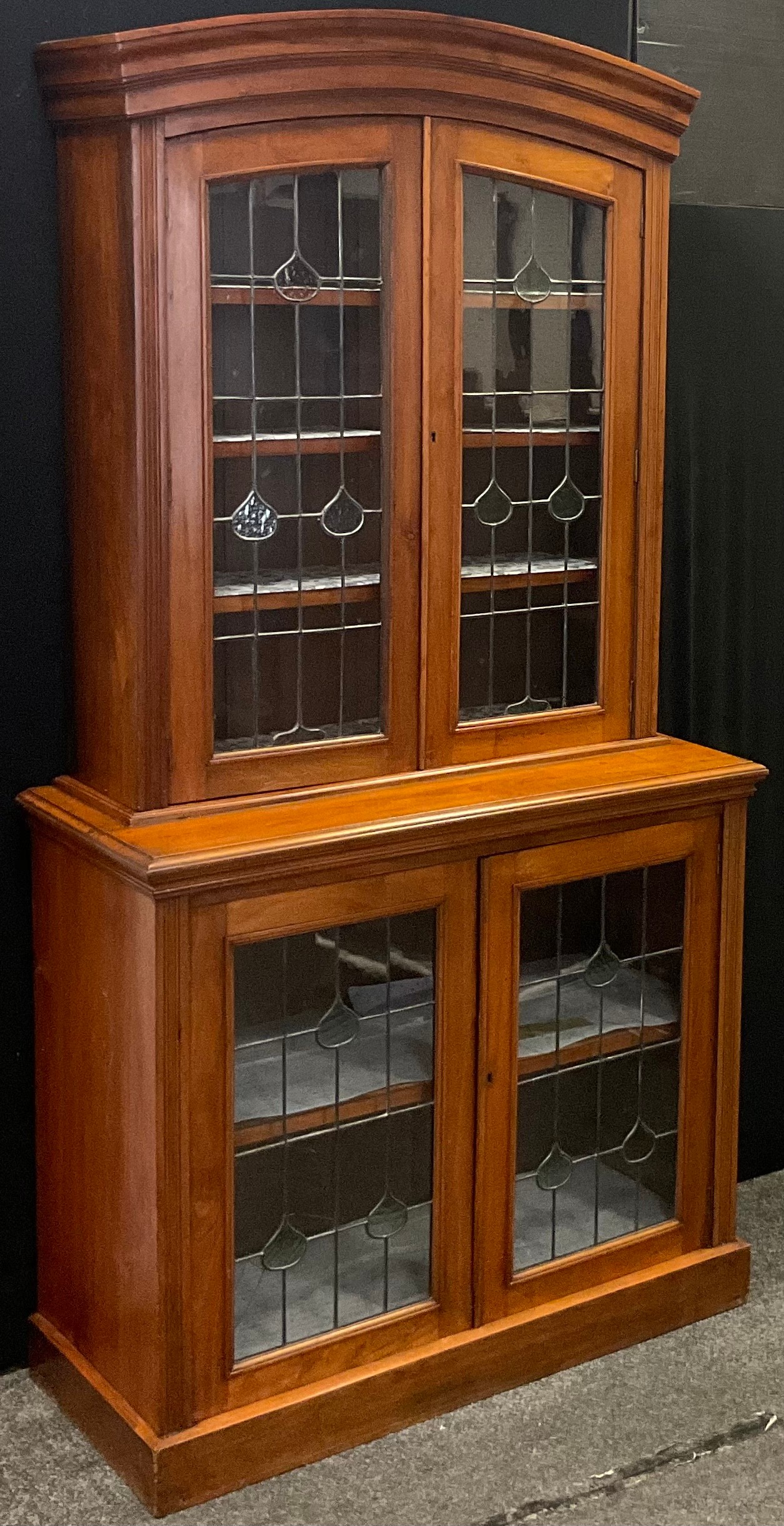 An Arts & Crafts walnut display cabinet, arched pediment above two leaded stained and clear glass