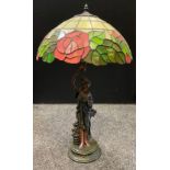 A Tiffany style leaded glass table lamp, the faux bronze base as a young lady collecting roses, 69cm