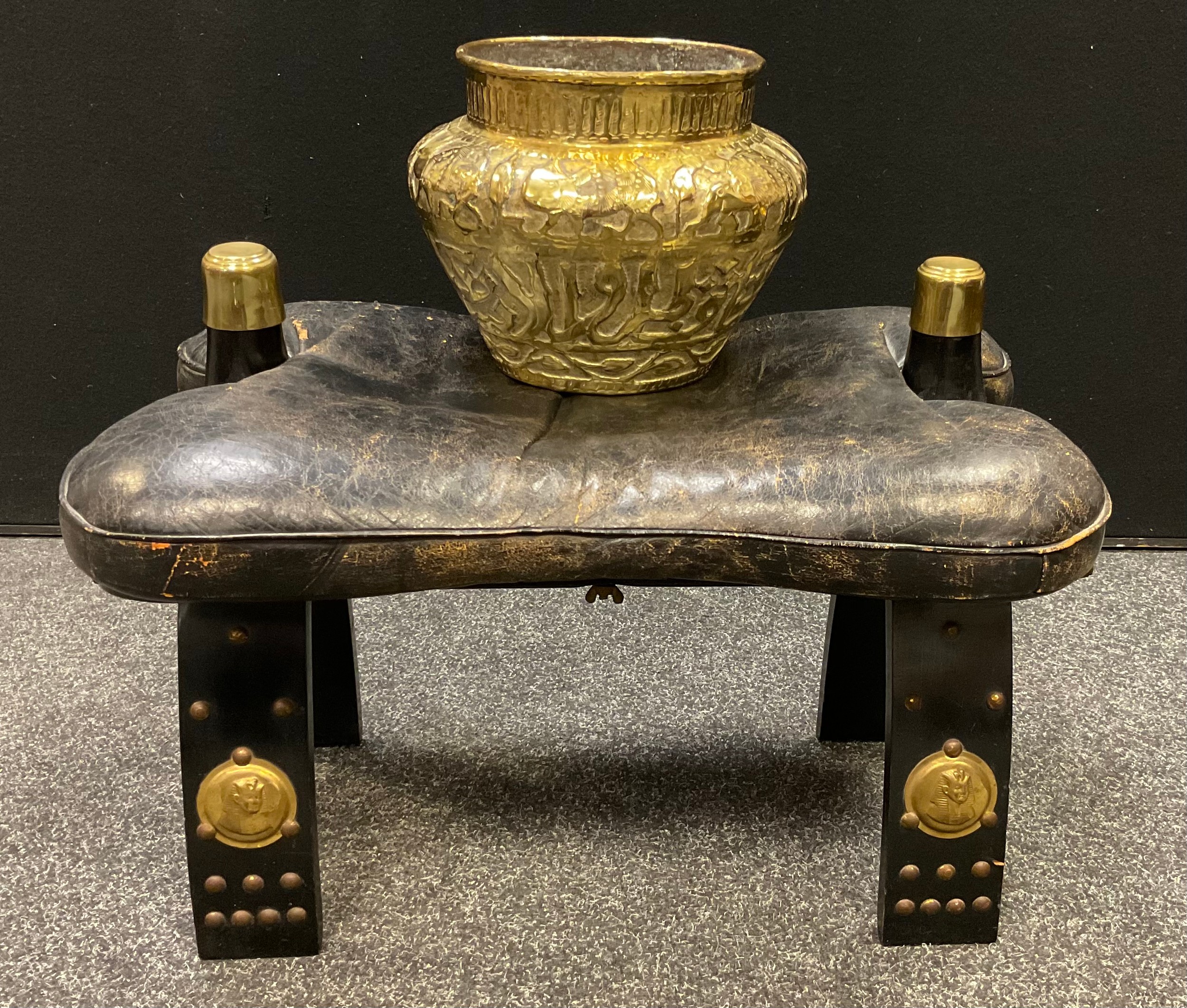 An early 20th century camel saddle stool, black leather seat cushion; a Middle Eastern hammered