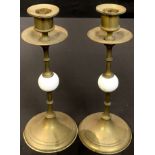 A pair of late 19th/early 20th century brass candlesticks, each with white porcelain knop and wide