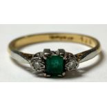 An 18ct gold diamond and emerald ring, the central cushion cut stone flanked by two brilliant cut