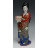 A Japanese porcelain figure, of a geisha, she stands, holding a lotus bowl, 23.5cm high