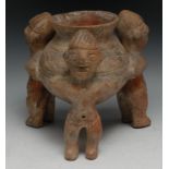 A South American terracotta vessel, with three figures standing holding a vase, 23cm high