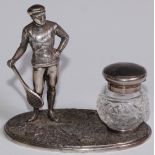 A silver plated novelty inkstand, as a gentleman dressed for tennis, glass well, 12.5cm wide