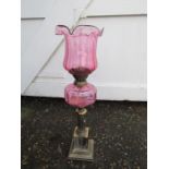 Oil lamp with brass base and cranberry coloured glass font and tulip shaped shade. Base has a hole