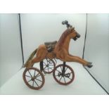 Minature carved wooden horse tricycle with metal stirrups, pedals and wheels with leather saddle,
