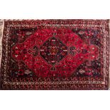 A Kashgai rug:, the brick red field with a central indigo hooked and shaped lozenge medallion,