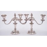 A pair of plated twin branch candelabra: with urn-shaped sconces having foliate borders on swept