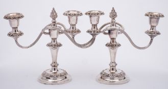 A pair of plated twin branch candelabra: with urn-shaped sconces having foliate borders on swept