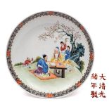 A Chinese famille rose saucer dish: enamelled with a sage and seated figure at a table in a garden,