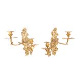 A pair of gilt brass twin branch wall appliques: the urn-shaped sconces mounted on swept foliate