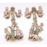 A pair of Dresden porcelain figural four-branch candelabra: modelled as bacchanalian putti around a