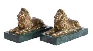 A pair of gilt brass recumbent lions: mounted on rectangular polished marble bases, 24cm long.