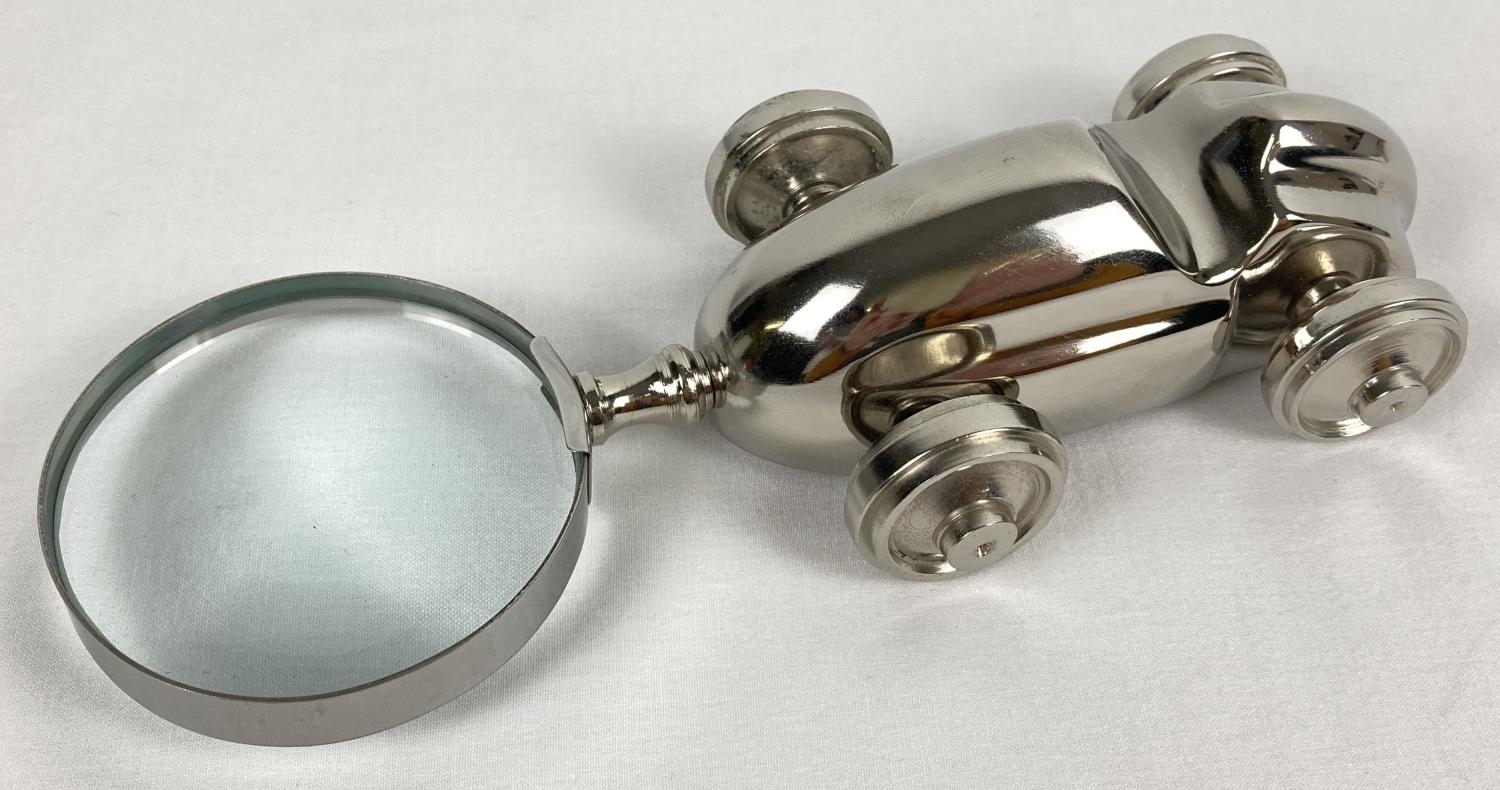 A magnifying glass with novelty shaped handle in the form of a racing car. With moving wheels.