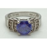 A silver cocktail ring set with purple/blue and clear cubic zirconia stones. Central round cut