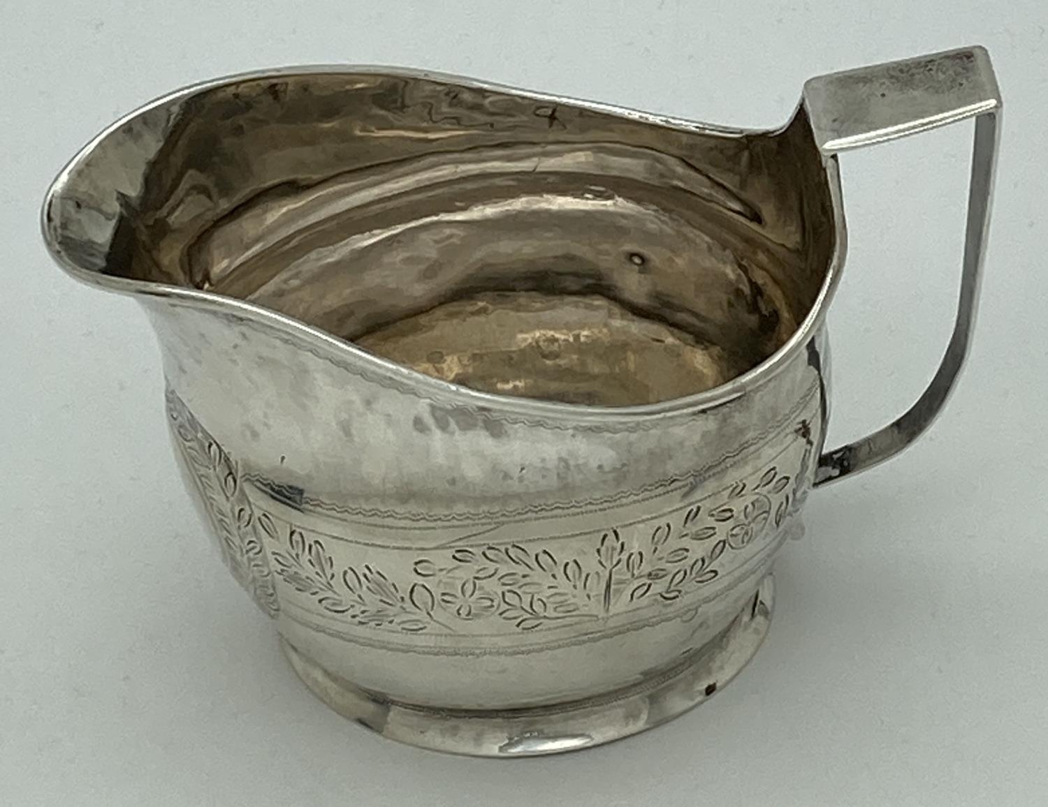 A Georgian silver cream jug with engraved floral banded design. Featuring a wreathed circular shaped