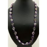 A dark and pale polished amethyst beaded necklace, approx. 24". With a white metal flower shaped T