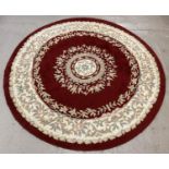 A vintage circular shaped Axminster floor rug with deep red ground. Pale pink, blue, green and beige