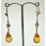 A pair of yellow metal drop earrings with faceted orange glass drops. Hooked wires, one with a