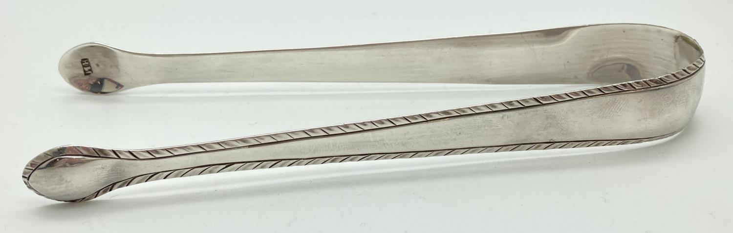 A pair of Georgian silver sugar tongs with feather edged detail. Stamped to inner spoon bowls with