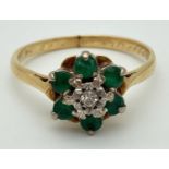 An 18ct gold, emerald and diamond ring set with flower shaped cluster. Central diamond surrounded by