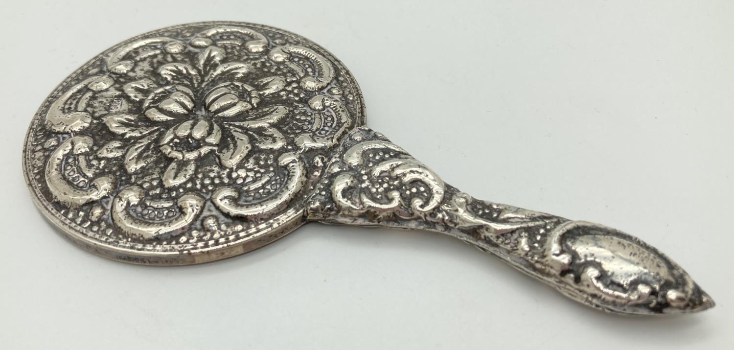 A small hand held 900 silver embossed mirror with scroll and foliate design. Approx. 14.5cm long,