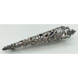 A white metal boutonniere in pierced work floral and scroll design. Secure pin back. Approx. 7cm
