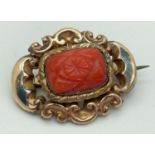 A Victorian yellow metal brooch set with carved coral stone, complete with safety chain. Tests as