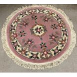 A vintage circular shaped Chinese style rug. Pink ground with floral design and tassled edge.