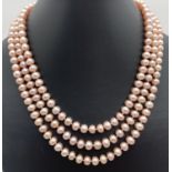 A 14" triple string of peach lustre freshwater pearls with large decorative box clasp. In the