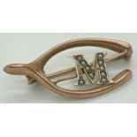 An Edwardian 9ct gold brooch in the form of a horseshoe, with central 'M' initial set with 10