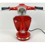 A novelty table lamp in the shape of the handlebars of a Vespa scooter, painted red. With moving