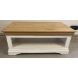 A modern cream painted coffee table with natural finish pine top. With undershelf and shaped base.