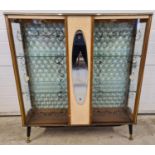 A mid century double door glass display cabinet with central mirrored panel. Pale green quilted